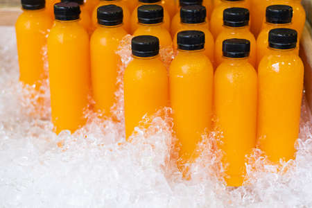 Bottles of fresh orange juice in a wooden bucket filled with ice.