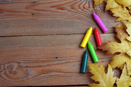 Wooden background with multicolored crayons and maple leavesの写真素材