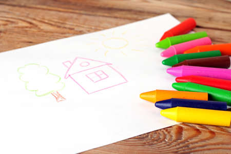 Oil pastel crayons lying on a paper with painted children's drawing. Copy space background. Selective focusの写真素材