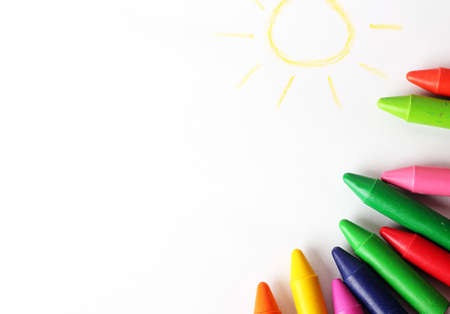Oil pastel crayons lying on a paper with painted children's drawing. Copy space background. Selective focusの写真素材