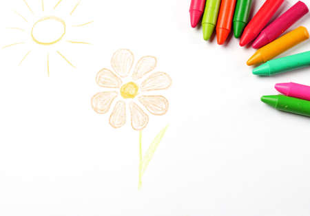 Crayons lying on a paper with children's drawing flower and sun. Selective focus, copy space backgroundの写真素材