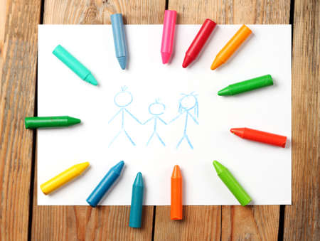 Crayons lying on a paper with children's drawing family. Selective focus, top viewの写真素材