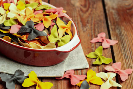 Raw, dry italian pasta in a ceramic bowl on a wooden background. Selective focus