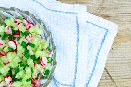 Still life, food and drink concept. Fresh spring salad with cucumbers, green onion and radish on a rustic wooden table. Selective focus, top viewの写真素材