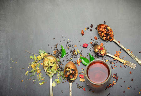 Still life, food and drink concept. Various kinds of tea with a glass of tea on a black chalkboard. Selective focus, copy space background, top view.の写真素材