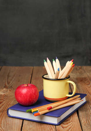 Still life, business, education concept. Pencils in a mug, book and apple on a wooden table with chalkboard. Selective focus, copy space, school backgroundの写真素材