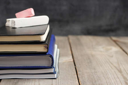 Still life, business, education concept. Notebook stack on a wooden table with chalk and chalkboard. Selective focus, copy space, school backgroundの写真素材