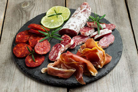 Assortment of spanish tapas or italian antipasti, jamon, prosciutto, chorizo, salami on a grunge black board, rustic style. Selective focusの写真素材