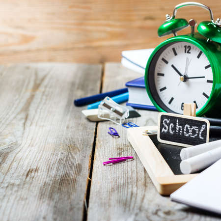Still life, business, education concept. Assortment of office and school supplies, alarm clock and chalkboard on a rustic wooden table. Selective focus, copy space backgroundの写真素材
