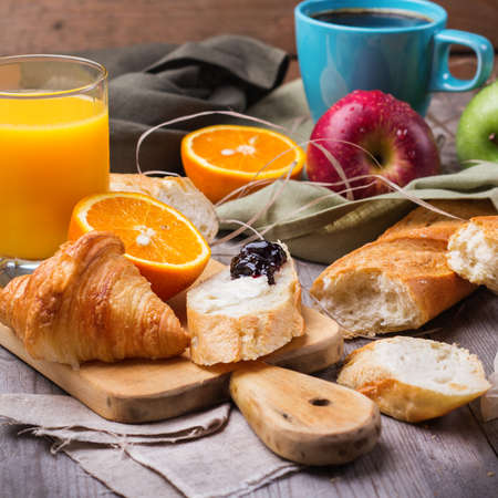 Still life, food and drink concept. French baguette with butter and jam, croissant, coffee, orange juice for breakfast on a rustic wooden table. Selective focusの写真素材