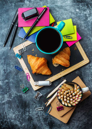 Education, back to school, business office breakfast concept. Stationery, supplies, croissant and mug of black coffee on a grunge chalkboard. Selective focus, copy space background, top view flat layの写真素材