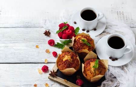 Still life, food and drink, breakfast concept. Fresh homemade muffins with raspberry and cups with coffee on a rustic white wooden table. Selective focus, copy space backgroundの写真素材