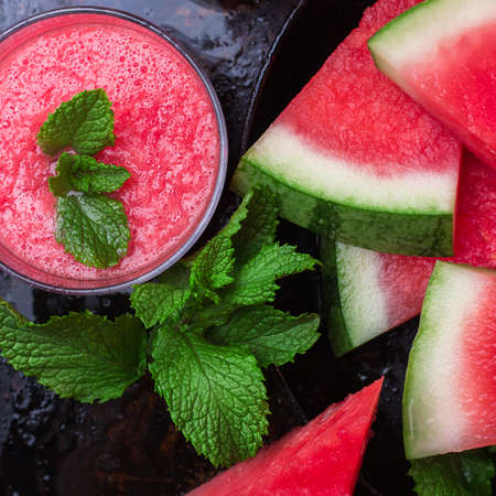 Still life, food and drink, diet concept. Organic fresh watermelon slices with mint and drink smoothie on a grunge black table. Selective focus, top view overhead flat layの写真素材