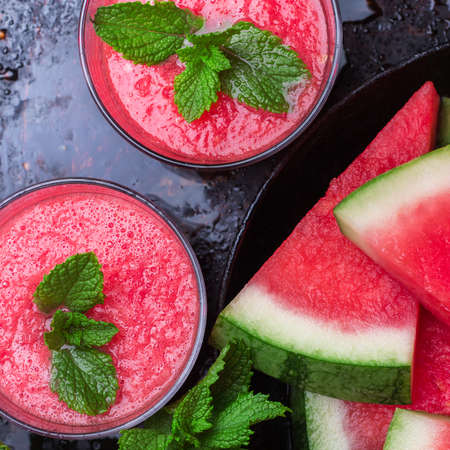 Still life, food and drink, diet concept. Organic fresh watermelon slices with mint and drink smoothie on a grunge black table. Selective focus, top view overhead flat layの写真素材