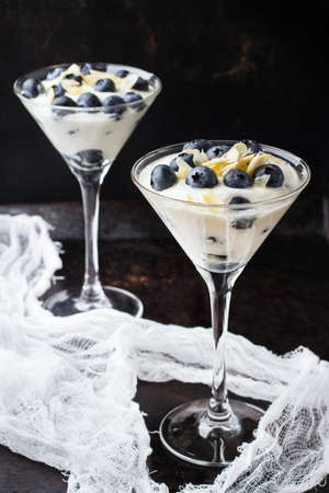 Healthy nutrition, breakfast concept. Homemade yogurt with granola muesli and blueberries in martini glass on a grunge rusty black table. Selective focusの写真素材