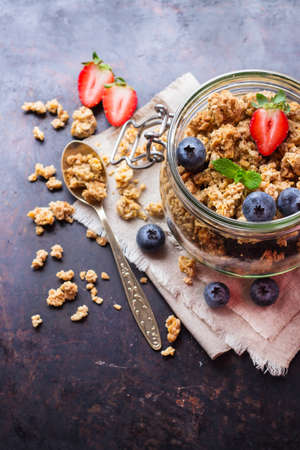 Breakfast, healthy food concept. Homemade muesli granola with berries in a jar on rusty black table. Selective focus, copy space backgroundの写真素材