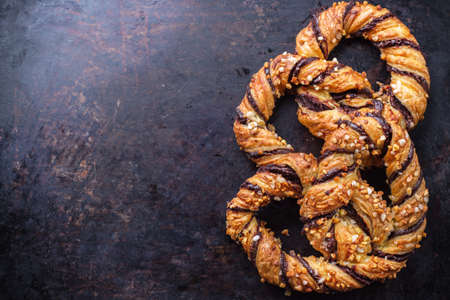 Homemade sweet pretzel with chocolate and crunchy almonds, traditional german bavarian treat on a black rusty table. Selective focus, copy space background, top view overhead flat layの写真素材
