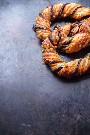 Homemade sweet pretzel with chocolate and crunchy almonds, traditional german bavarian treat on a black rusty table. Selective focus, copy space backgroundの写真素材