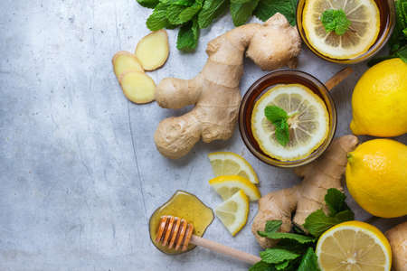 Ginger tea in a glass with lemon, mint and honey. Hot drink for cold flu winter autumn on a rustic metal table. Selective focus, copy space background, top view flat layの写真素材