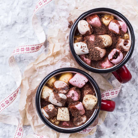 Hot chocolate in red mugs with marshmallows and spices on rustic christmas table. Selective focus,...