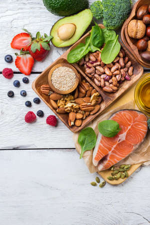 Selection of healthy food for heart, salmon fish avocado olive oil pumpkin seeds nuts broccoli green spinach berries on a white rustic wooden table. Copy space background, top view flat lay overheadの写真素材