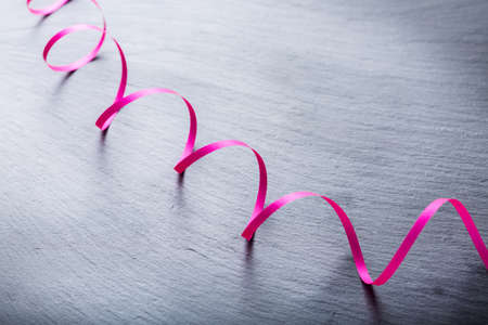 Love and still life concept. Holiday gift present concept with pink ribbon on a grunge black table....