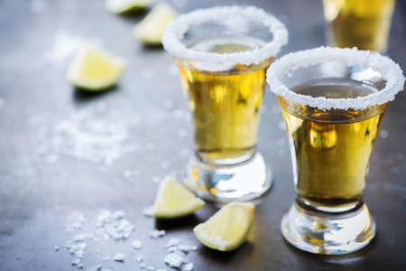 Alcohol, junk food, party, holidays concept. Golden mexican tequila shot on a grunge black table...