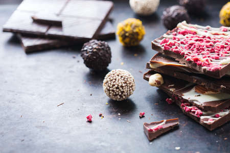 Sweet and treat, junk unhealthy food. Assortment of chocolate bar and praline truffle on black moody grunge table. Copy space backgroundの写真素材