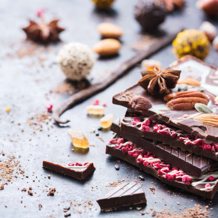 Sweet and treat, junk unhealthy food. Assortment of chocolate bar and praline truffle with spices and nuts on black moody grunge tableの写真素材