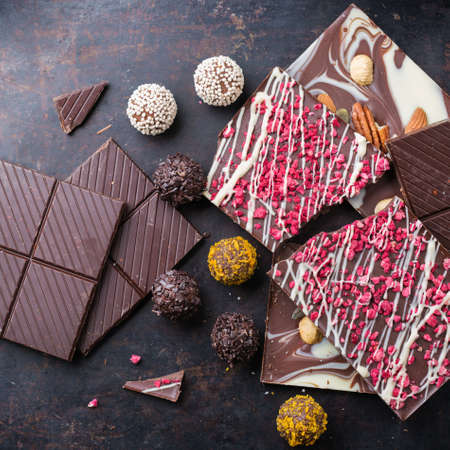 Sweet and treat, junk unhealthy food. Assortment of chocolate bar and praline truffle on black moody...