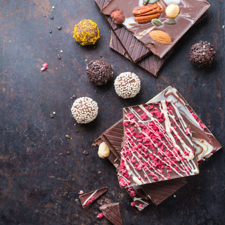 Sweet and treat, junk unhealthy food. Assortment of chocolate bar and praline truffle on black moody grunge table. Top view flat lay overheadの写真素材