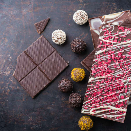 Sweet and treat, junk unhealthy food. Assortment of chocolate bar and praline truffle on black moody...