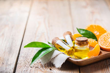 Health and beauty, still life concept. Organic essential tangerine, mandarin, clementine oil in a small glass jar with green leaves and orange fruit on a rustic wooden table. Copy space backgroundの写真素材
