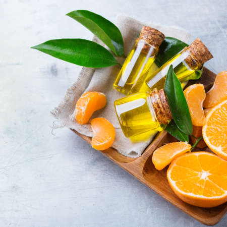 Health and beauty, still life concept. Organic essential tangerine, mandarin, clementine oil in a small glass jar with green leaves and orange fruit on a table. Top viewの写真素材