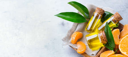 Health and beauty, still life concept. Organic essential tangerine, mandarin, clementine oil in a small glass jar with green leaves and orange fruit on a table. Top view, copyの写真素材