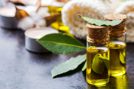 Healthy lifestyle concept. Natural bay laurel essential oil, essence in glass bottle with leaves, towels and candle on a rusty black table for beauty, spa, therapyの写真素材