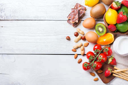 Selection of allergy food, orange citrus juice milk red tomato strawberry kiwi eggs chocolate nuts bread gluten on a rustic wooden table. Copy space background, top view flat lay overheadの写真素材