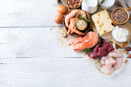 Assortment of healthy protein source and body building food. Meat beef salmon chicken eggs dairy products milk cheese yogurt beans quinoa nuts oat meal. Copy space background, top view flat layの写真素材