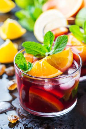 Traditional cold spanish sangria cocktail with red wine and ingredients on a black table, citrus fruit orange lime lemon mint leaves and ice for hot summer daysの写真素材