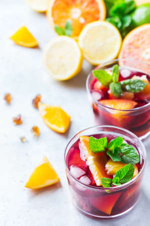 Traditional cold spanish sangria cocktail with red wine and ingredients on a white table, citrus fruit orange lime lemon mint leaves and ice for hot summer daysの写真素材