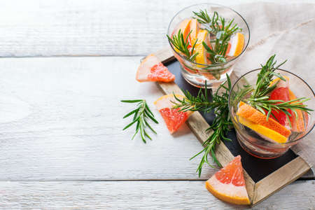 Healthcare, fitness, healthy nutrition concept. Fresh cool grapefruit rosemary infused water, cocktail, detox drink, lemonade for spring summer days on a white wooden table. Copy space backgroundの写真素材
