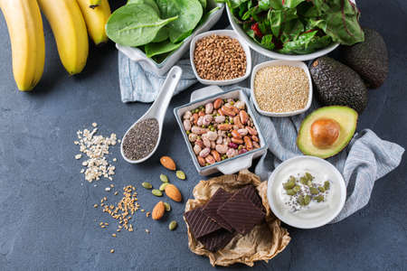 Healthy food nutrition dieting concept. Assortment of high magnesium sources. Banana chocolate spinach chard, avocado, buckwheat, sesame chia flax seeds, yogurt, nuts, beans oatの写真素材