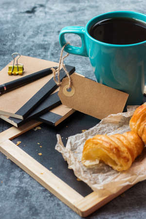 Education, business office breakfast concept. Stationery, supplies, pencil, pen, note, croissant and mug of black coffee on a grunge chalkboardの写真素材