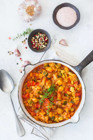 Healthy homemade vegan food concept. Stew organic vegetables ragout french ratatouille in frying pan on a white cozy kitchen table. Top view flat lay backgroundの写真素材