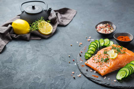 Raw salmon fillet with lemon and cucumber for preparation japanese food, rolls, sushi, maki. Ingredients on a dark kitchen table, copy space background.の写真素材