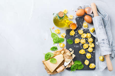 Assortment of italian food and ingredients, handmade tortellini with green spinach and cheese on a cutting board on a kitchen table. Top view flat lay copy space backgroundの写真素材