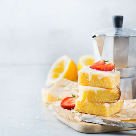 Food, breakfast teatime concept. Homemade lemon polenta cookie bars with white icing on a kitchen table with coffee. Copy space backgroundの写真素材