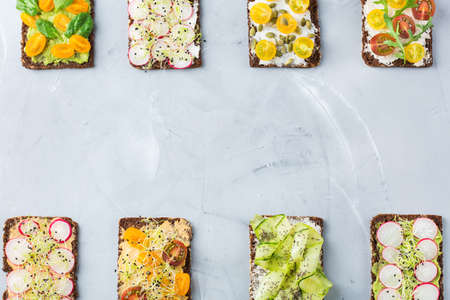 Food and drink, still life concept. Variety of handmade sandwiches with cream cheese, hummus, avocado, vegetables and micro greens sprouts for lunch table. Top view flat lay copy space backgroundの写真素材