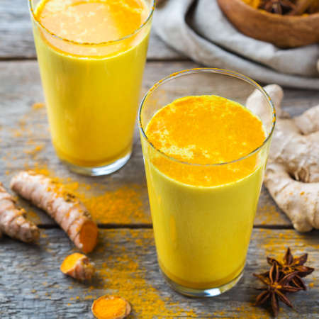 Traditional indian drink turmeric golden milk in a glass with ingredients, ginger, curcuma, honey on a rustic wooden tableの写真素材