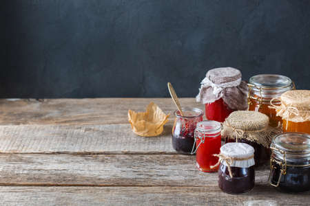 Food and drink, harvest summer autumn concept. Assortment of seasonal berries and fruits jams in jars on a wooden table. Copy space rustic backgroundの写真素材